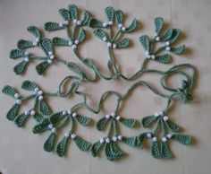 crocheted green leaves and white beads arranged in the shape of a circle on a table