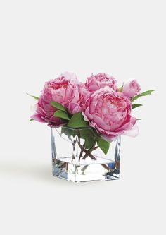 some pink flowers are in a glass vase on a white surface with green leaves and stems