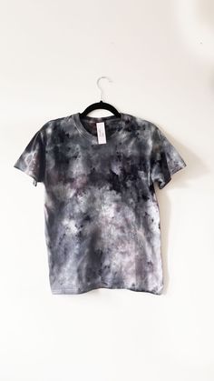 a t - shirt hanging on a hanger against a white wall with a black and grey tie dye pattern