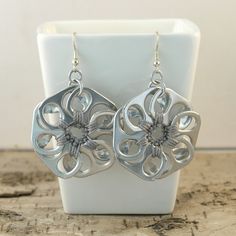 a pair of silver flower earrings sitting on top of a white display stand next to a wall