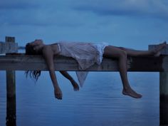 a woman laying on top of a wooden pier next to the ocean with a message written below her