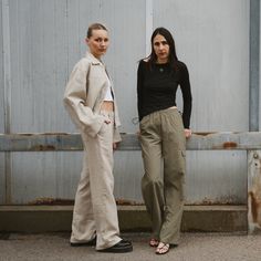 two women standing next to each other in front of a metal wall with peeling paint on it