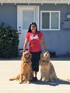 a woman standing next to two dogs in front of a house