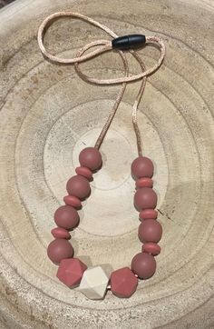 a red and white beaded necklace sitting on top of a wooden bowl next to a black cord