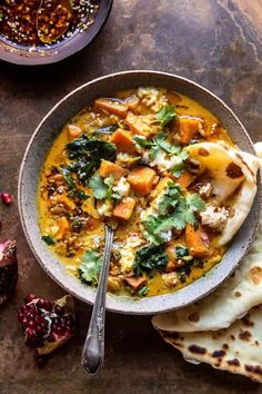 a bowl filled with soup next to pita bread and pomegranates