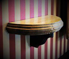 a wooden shelf mounted to the side of a pink and white striped wall next to a mirror