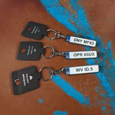 three black and white keychains with tags attached to them on a brown surface