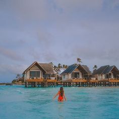 a woman wading in the ocean next to some wooden houses on stilfets