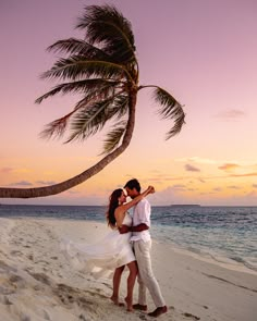 a man and woman standing on top of a sandy beach next to a palm tree