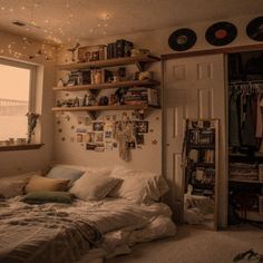 an unmade bed sitting next to a window with lots of books on the shelves