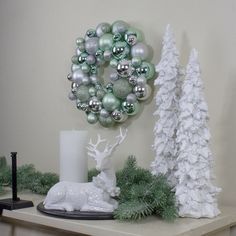 christmas decorations on a mantle with white and green ornaments around the wreath, candlesticks and deer figurines