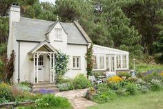 a small white house surrounded by trees and flowers