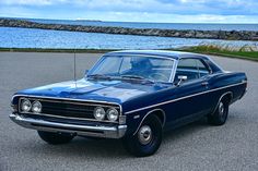 an old blue car is parked by the water