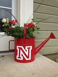 a red watering can with flowers in it sitting on the side of a house next to a window