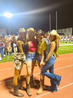 three women in cowboy hats pose for a photo at a baseball game on the field