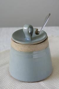 a ceramic container with a spoon in it on a white tablecloth covered table cloth