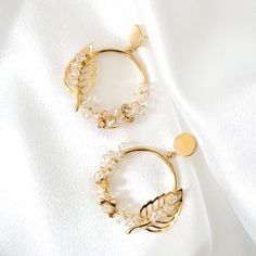 What a beautiful, delicate testament to nature. These stunning lightweight statement earrings gracefully capture the essence of the natural world with their shimmering earthy tones. Featuring a 24-karat gold plated loop and round flat posts, these earrings are adorned with generously sparkling hand-wired Swarovski crystals in delicate clear and gold finishes. Additionally, a beautiful leaf filigree adorns the loop, symbolizing the golden fall of leaves. Romantic, sophisticated, and darling, these earrings are a charming addition to any ensemble. Style E624 Piece approximate measurements: - each earring is 1.9" long - at its widest 1.75" Materials: - 24 karat gold plated brass loops, posts and leaves - Swarovski crystals in classy gold and sparkling crystal clear finish - gold-plated artist Artistic Wire, Loop Earrings, Vintage Elegant, Sparkling Crystal, Earthy Tones, Ear Studs, Statement Earrings, Handmade Natural, Jewelry Pieces