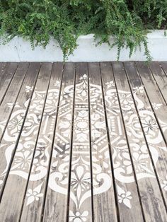 a wooden deck with an intricate design painted on the floor next to green plants and shrubbery