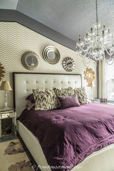 a bedroom with purple bedding, chandelier and two mirrors on the wall