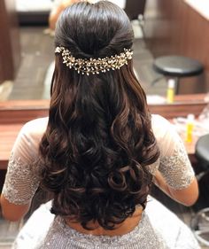 the back of a woman's head with long, curly hair and gold jewelry