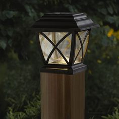 a light that is on top of a wooden post in front of some bushes and trees