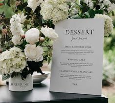 a table with white flowers and a menu on it next to a vase filled with greenery