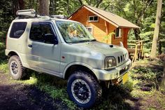 an suv parked in the woods next to a small cabin with a dog on top