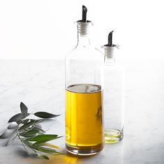 two bottles filled with olive oil on top of a table next to an olive branch