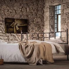 a bedroom with stone walls and flooring has an iron bed frame in the middle