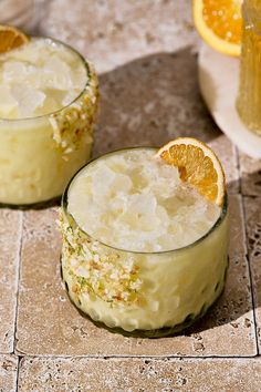 two glasses filled with ice and orange slices on a tile floor next to each other