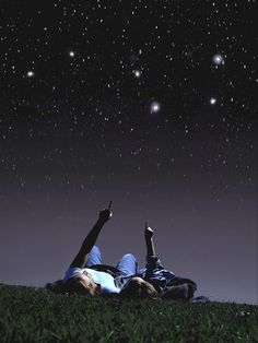 two people laying on the grass under stars in the night sky with their hands up