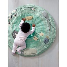 a baby laying on top of a green rug with animals and jellyfishs around it