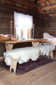 a wooden table and bench in a room with wood flooring, white fur on the rug