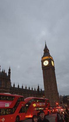 two people are standing in front of the big ben clock tower and red double decker buses