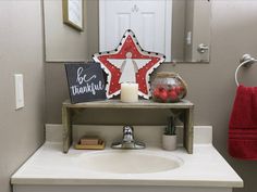 a bathroom sink with a wooden star sign above it and a red towel hanging on the wall