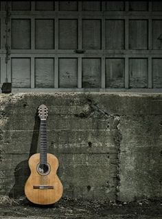 an acoustic guitar leaning against a concrete wall