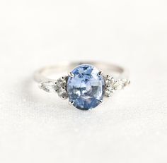 an oval blue and white sapphire ring with three diamonds on the sides, set in 18k white gold