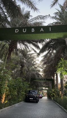 two cars are parked under a sign that says dubai in front of some palm trees