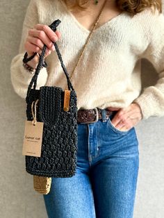 a woman is holding a black purse with a tag on it and she has her hands in her pockets