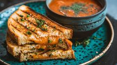 a grilled cheese sandwich with tomato soup on the side is served on a blue plate