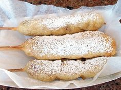 two pastries on sticks covered in powdered sugar sitting on top of wax paper