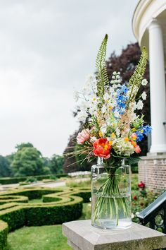 a vase filled with colorful flowers sitting on top of a stone bench next to a garden