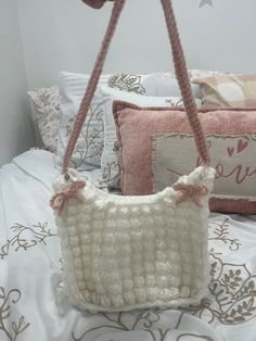 a crocheted purse sitting on top of a bed next to pillows and pillow cases