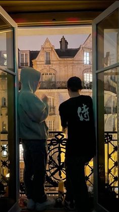 two young boys standing in front of an open window looking out at the city below