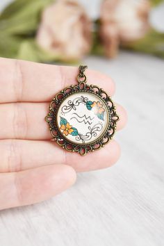 Your zodiac necklace collection is not complete without a Aquarius necklace water sign. Handmade with whimsical, cute miniature art and a vintage style, this Aquarius pendant ignites your inner magic. The Aquarius jewelry is painted by hand, making each piece unique and one of a kind, just like you. Click through to see more glass pendant necklaces! Aquarius Pendant Necklace