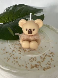 a small teddy bear sitting on top of a cake next to a green monster leaf