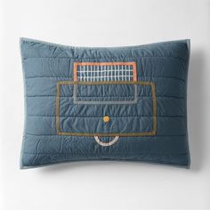 a blue pillow with a tennis racket embroidered on the front and back, sitting against a white wall