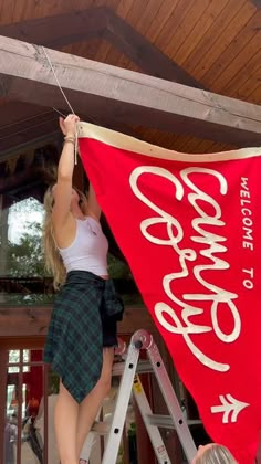 two women are hanging a red banner on a wooden structure while another woman is standing up in the background