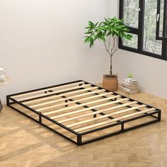 a bed frame sitting on top of a wooden floor next to a potted plant