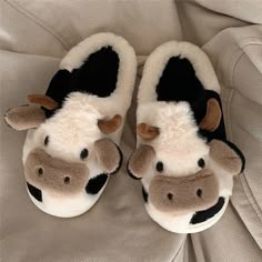 a pair of slippers with a cow design on the front and bottom, sitting on a bed sheet